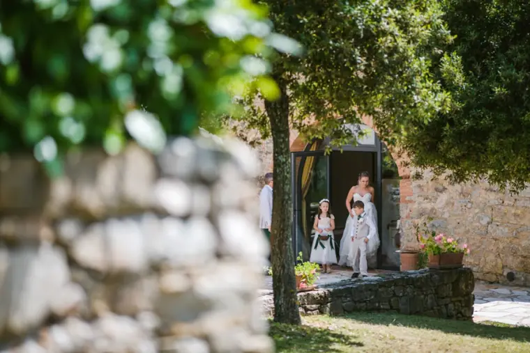 Bride and flower girls emerging from a stone doorway, framed by a blurred wall