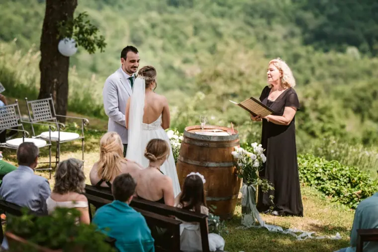 Celebrant leading the ceremony as guests watch from benches on the hillside, Livernano Estate