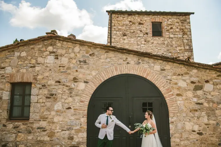 Groom twirling his bride in front of an arched door of a stone farmhouse at Livernano Estate