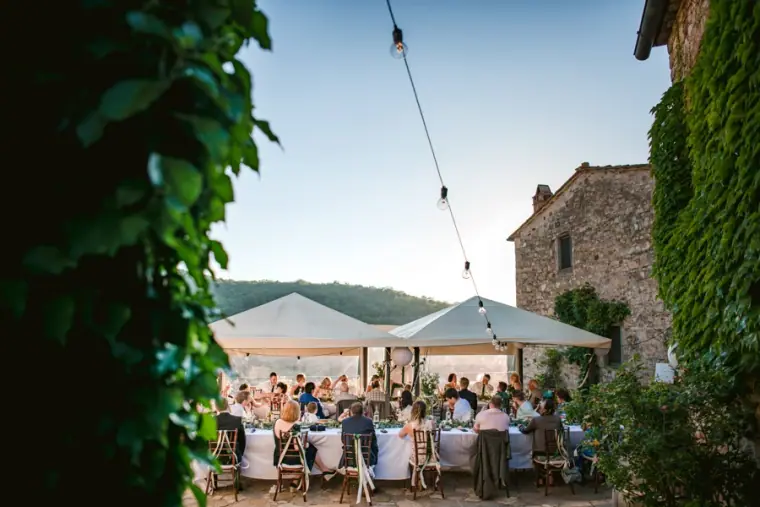 Guests dining under white canopies and festoon lights beside a stone tower at Livernano Estate