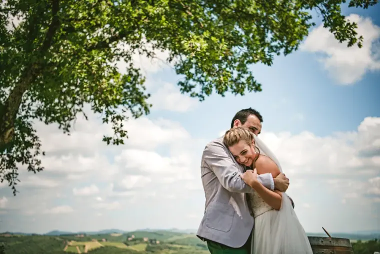 Bride hugging her groom from behind with Tuscan hills and blue sky beyond