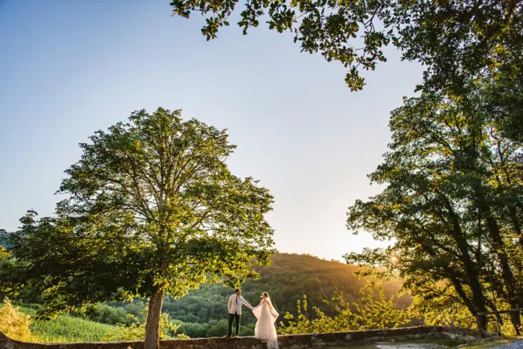 Bride and groom small beneath tall trees on a hilltop at golden hour, Livernano Estate