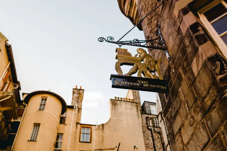 Gilded hanging pub sign above tall sandstone buildings in Edinburgh's Old Town