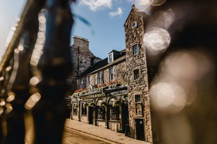 Stone pub and tower glimpsed past blurred iron railings in Edinburgh's Old Town