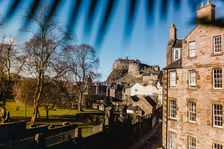 Edinburgh Castle beyond bare trees and old stone tenements on a sunny day