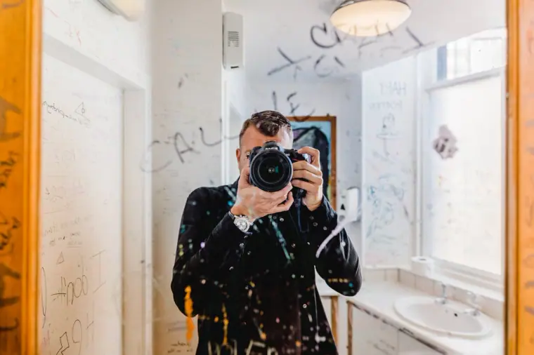 Photographer taking a mirror selfie in a graffiti-covered café washroom