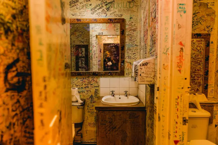 Graffiti-covered washroom with a mirror, sink and framed picture, in warm light