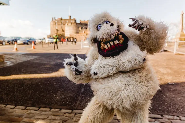 Street performer in a shaggy white monster costume pulling a scary face near Edinburgh Castle