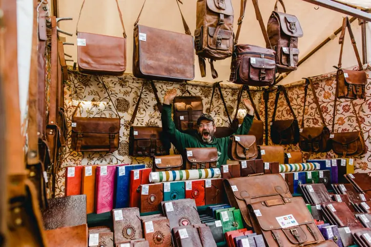 Market stall packed with leather satchels and notebooks, its stallholder peeking out