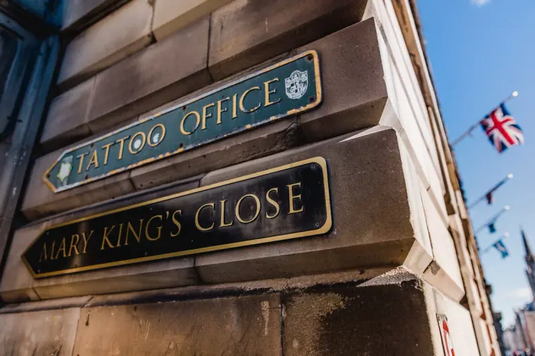 Street signs for Mary King's Close and a tattoo office on a stone wall, Edinburgh