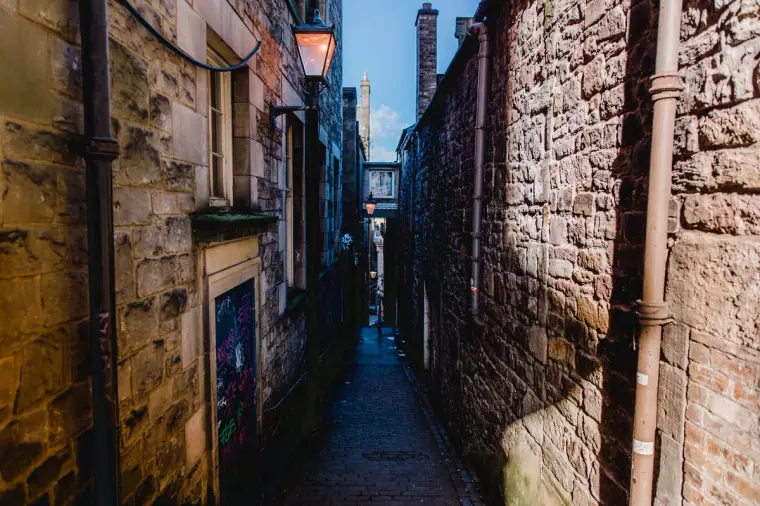 Narrow stone alleyway between tall buildings leading to a bridge, Edinburgh