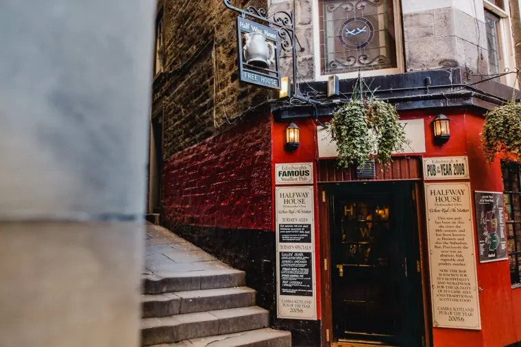 Red-painted traditional pub front with hanging baskets beside a stone stairway
