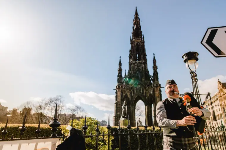 Kilted bagpiper playing on Princes Street with the Scott Monument behind