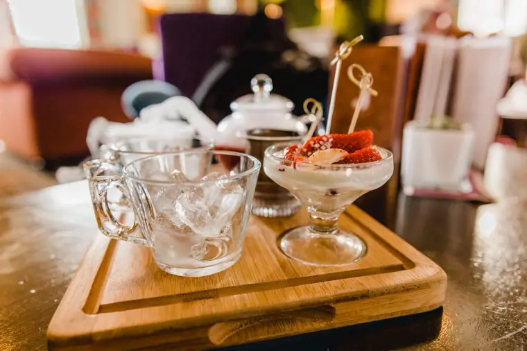 Glass teacups, a teapot and a strawberry dessert on a wooden serving board