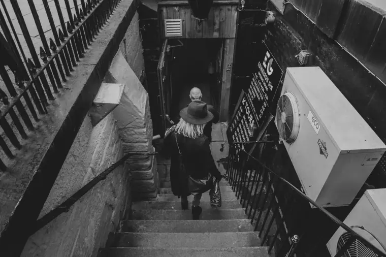 Black-and-white shot of a woman descending steep stone steps to a basement entrance