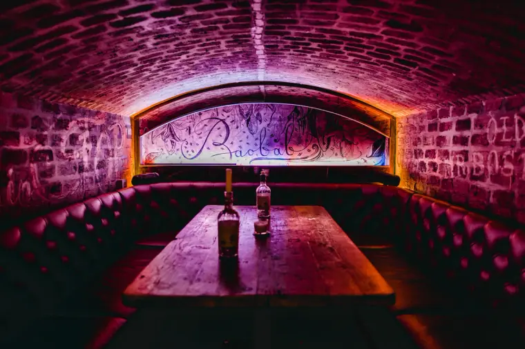 Vaulted cellar bar with red leather booths and pink lighting