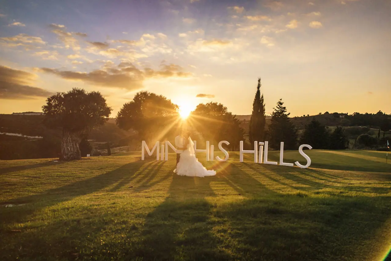 Katie and Paul silhouetted on the golf course lawn at sunset, with Minthis Hills text overlay