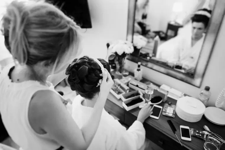 Black-and-white shot of a bridesmaid having her hair styled at a hotel dressing table
