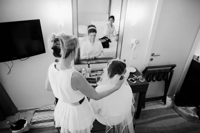 Black-and-white view of a bridesmaid's hair being pinned as she sits by a mirror