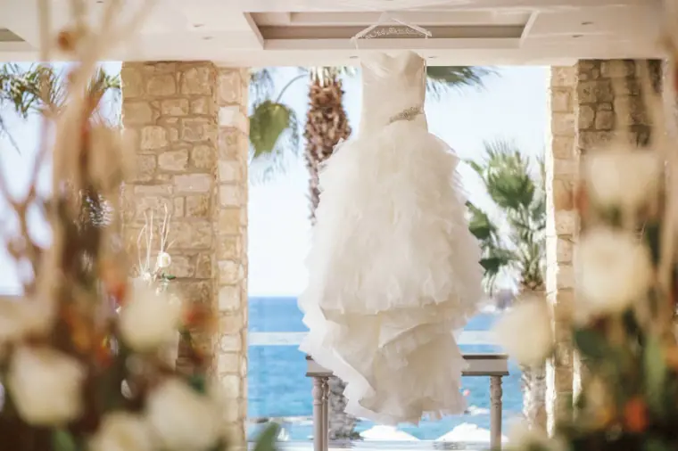 Wedding dress hanging between stone pillars with palm trees and sea beyond
