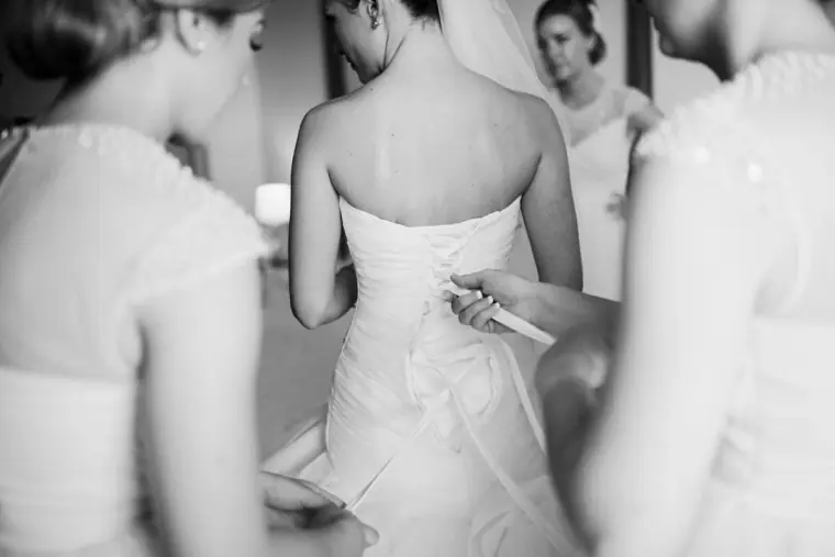 Black-and-white shot of bridesmaids lacing up the back of the bride's strapless gown