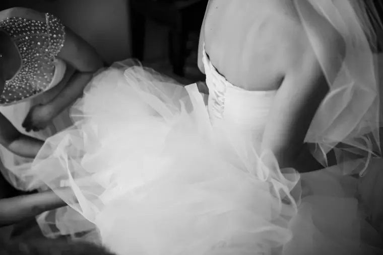 Black-and-white close-up of the bride's tulle skirt and corset being adjusted