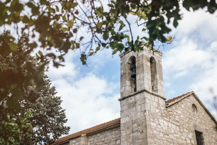 Stone bell tower beneath leafy branches and blue sky at Minthis Hills