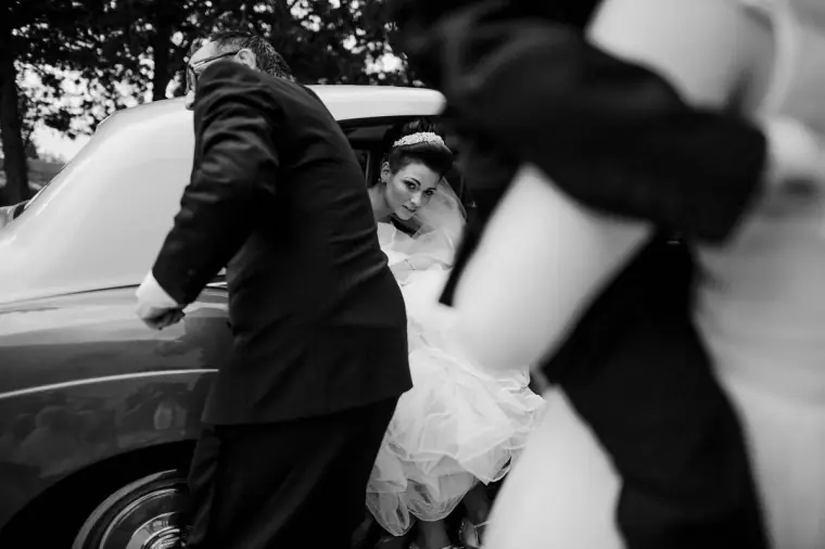 Black-and-white shot of the bride being helped out of a vintage car