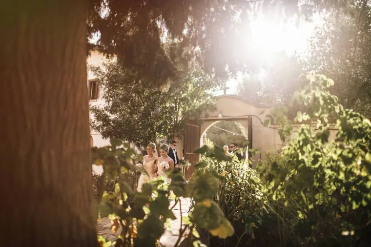 Bride arriving at the arched gateway in hazy sunlight through the trees