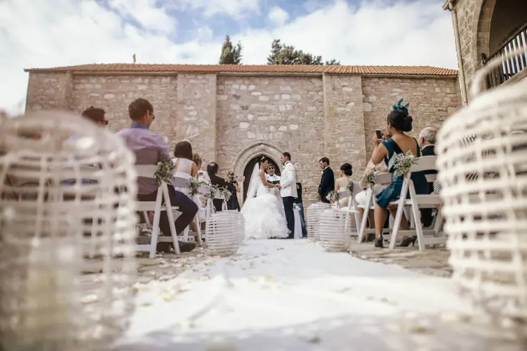 Low view down the aisle between wicker lanterns to the couple at the altar