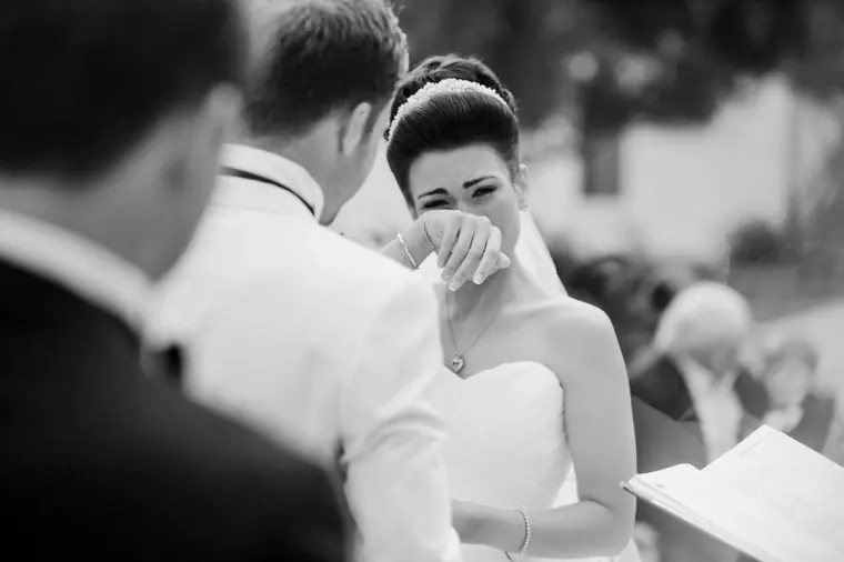 Black-and-white shot of the bride wiping away a tear during the vows