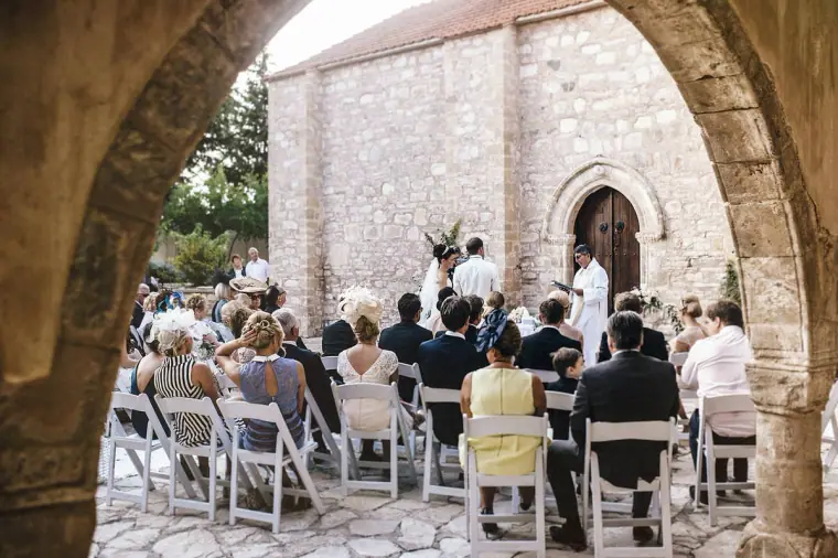 Ceremony in front of the old stone chapel seen through a stone archway, Minthis Hills