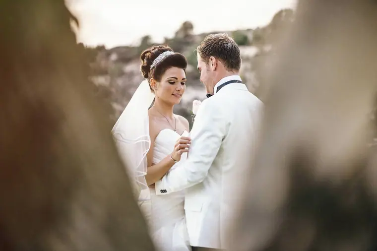 Newlyweds smiling together, framed by blurred tree trunks