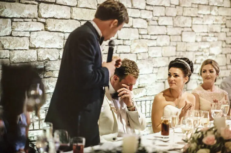 Best man with a microphone resting a hand on the groom's head during his speech
