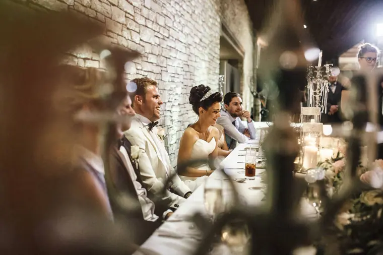 Top table laughing during speeches, seen past a blurred candelabra