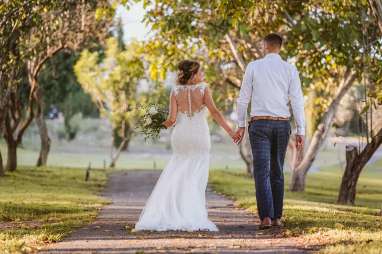 Bride and groom walking hand in hand down a path between olive trees