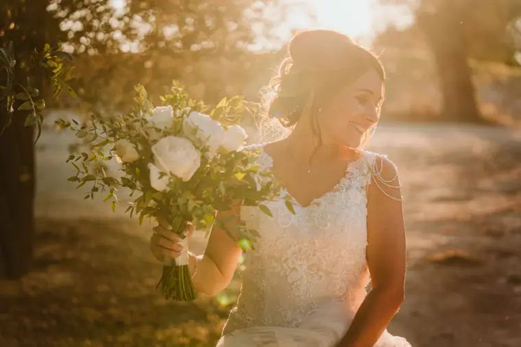 Bride smiling over her shoulder holding her bouquet in warm sunlight