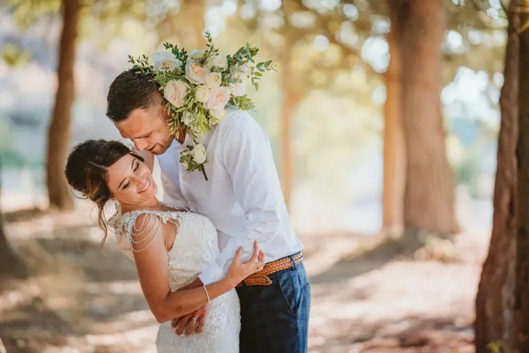 Groom kissing his laughing bride's forehead among the pines at Minthis Hills