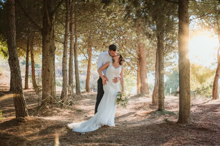Groom hugging his bride from behind in a sunlit pine wood