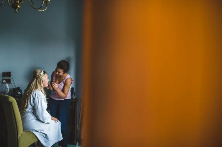Bride in a white robe having her make-up done in the hotel bedroom