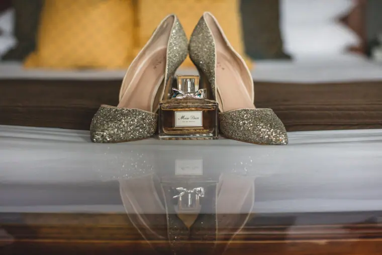 Glittery gold bridal heels and a perfume bottle on a glossy surface