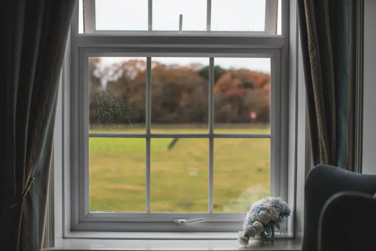 Sash window looking out onto a green lawn and autumn trees, bouquet on the sill