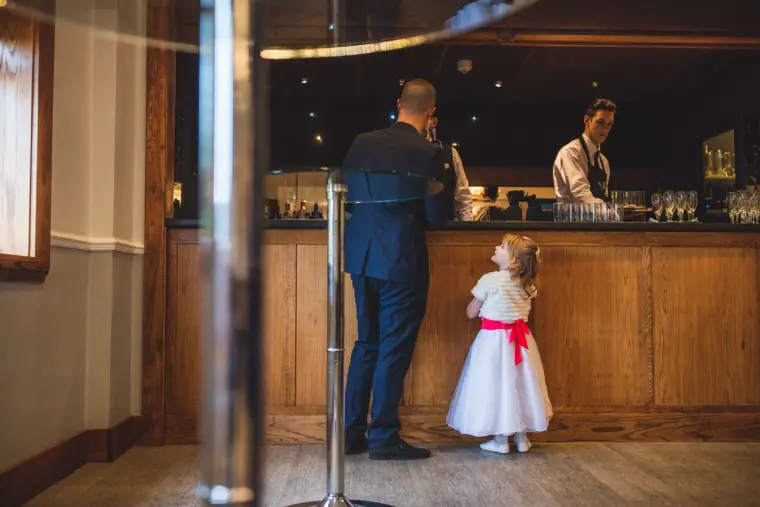 Groom at the hotel bar beside a little girl in a white dress with a red sash