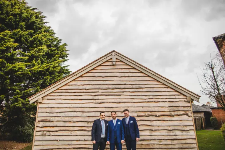 Groom and groomsmen in navy suits standing in front of a timber barn