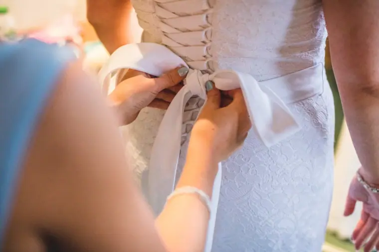 Bridesmaid tying the satin bow on the back of the bride's corset dress