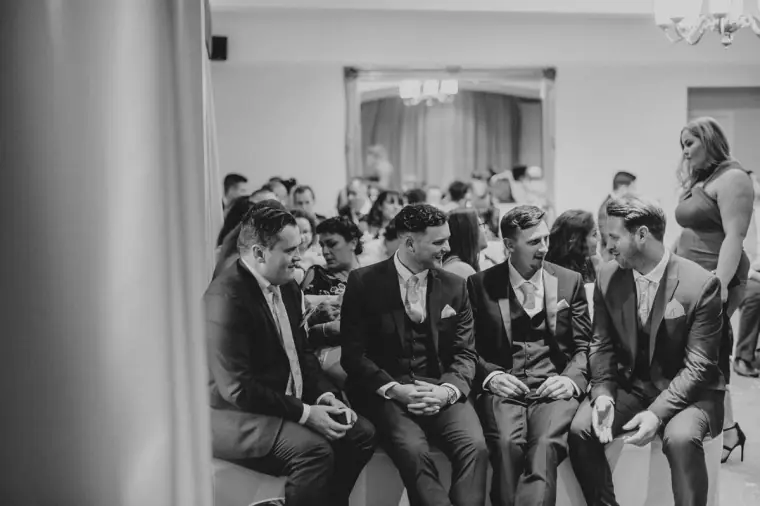 Black-and-white shot of the groom and groomsmen seated, waiting for the ceremony