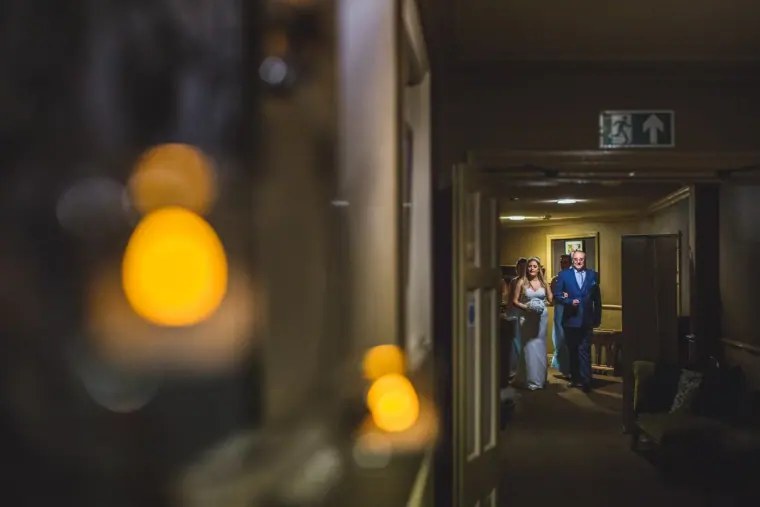 Bride and her father waiting at the end of a corridor, glowing lights in the foreground