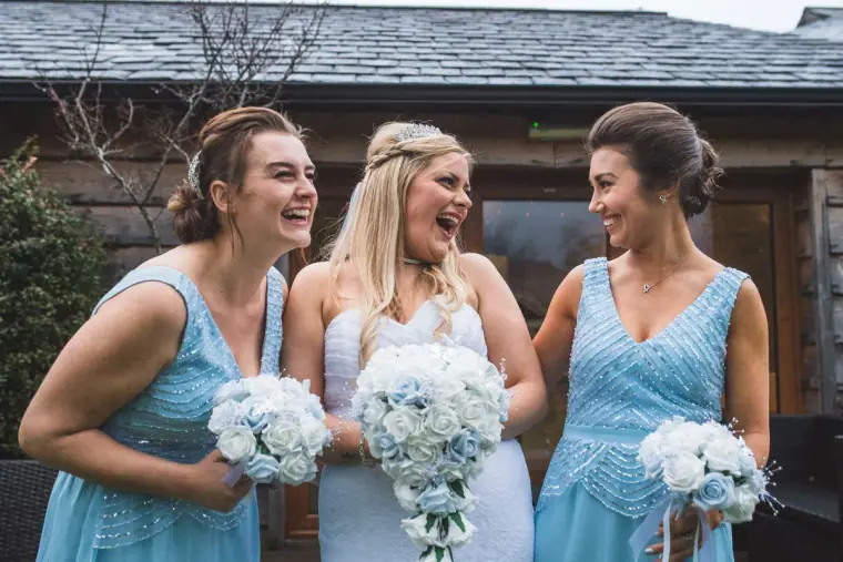 Bride laughing with two bridesmaids in pale blue holding white bouquets