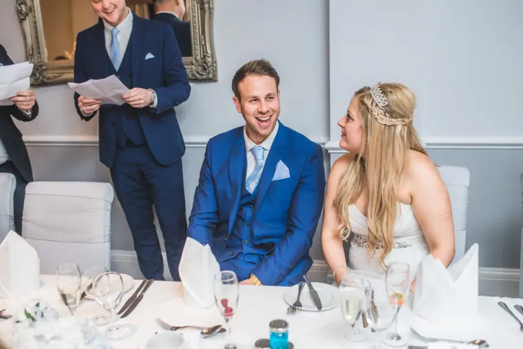 Groom laughing at the top table beside his bride as the best man reads his speech