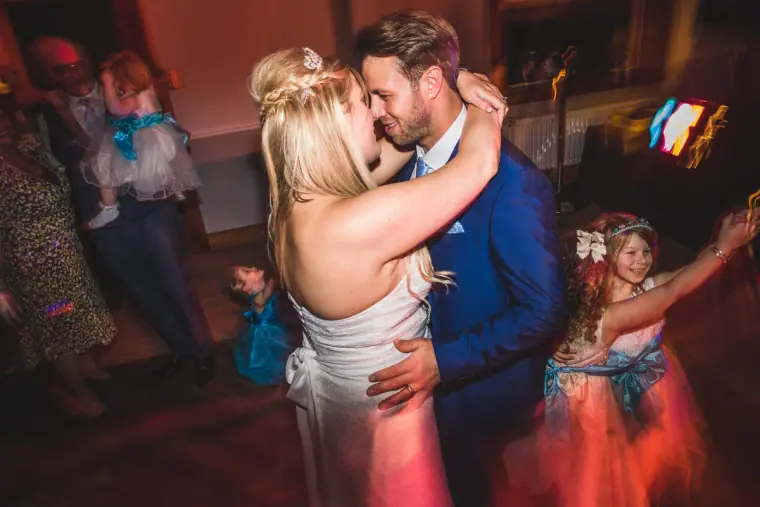 Bride and groom kissing on a busy dance floor with guests dancing around them